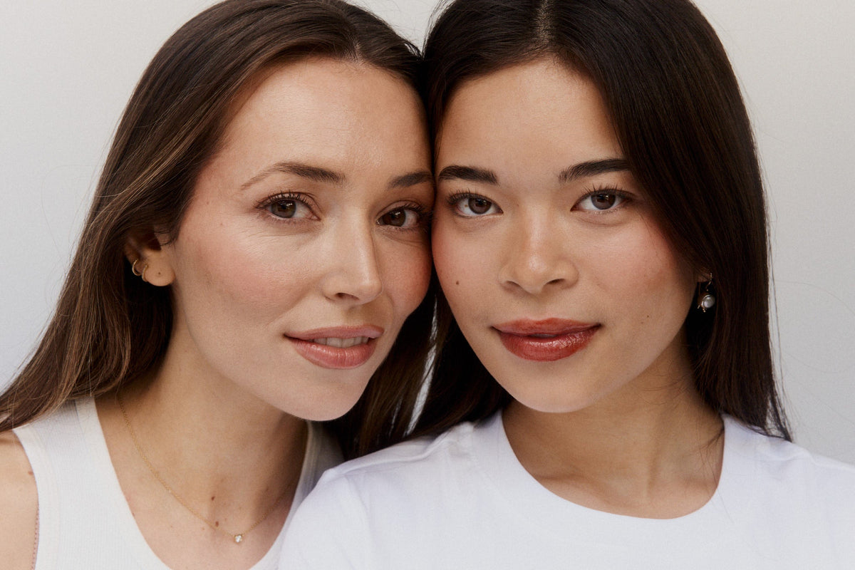 Two women in white tops with glowing skin, heads leaning together