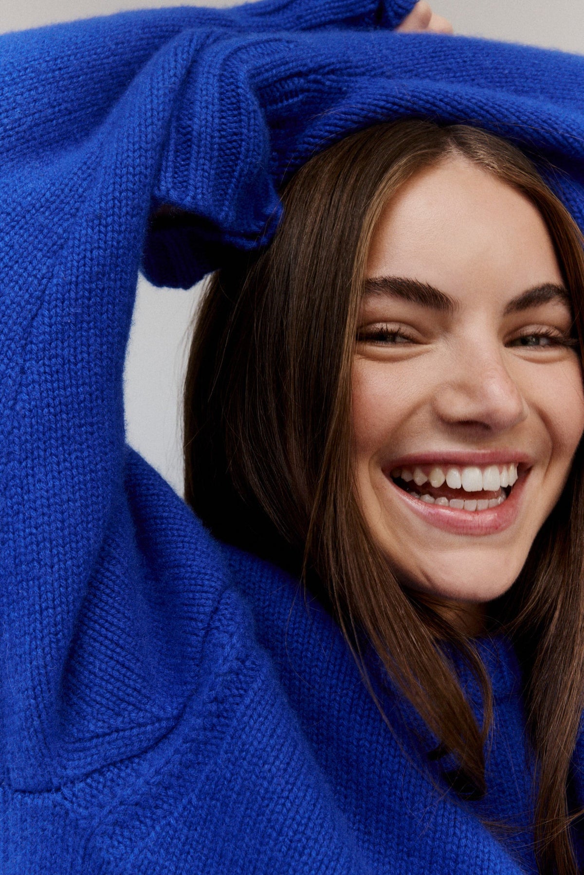 Laughing woman in a cobalt blue sweater with her arms raised over her head