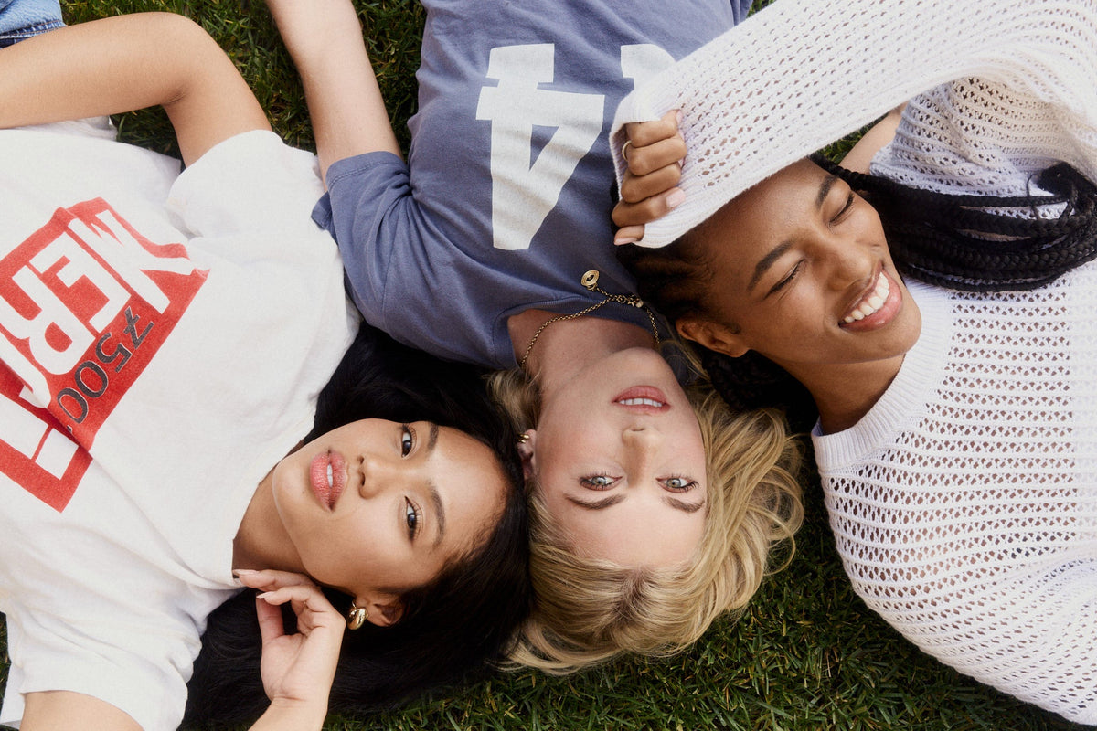 Three friends lying head to head on the grass, smiling