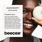 A smiling woman holds a round beige cleansing bar against her face next to a white text card detailing the 'Well-Rounded Bar' by beecee.