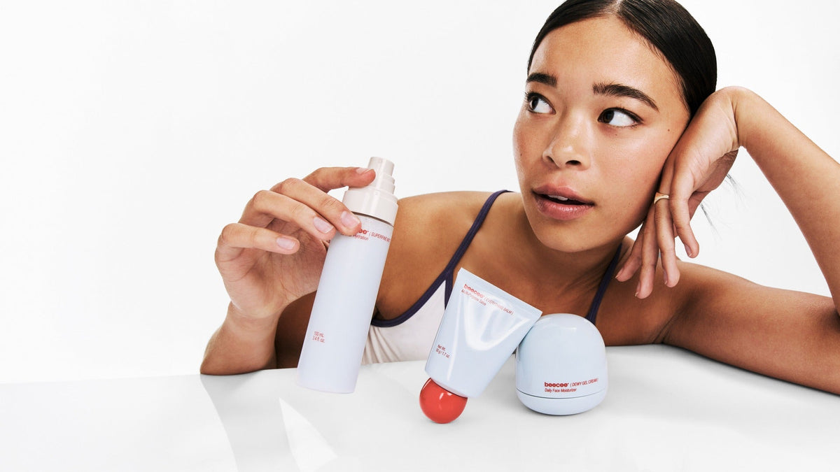 Woman leaning on a white table, holding Superfine Mist beside Everything Balm and Dewy Gel Cream